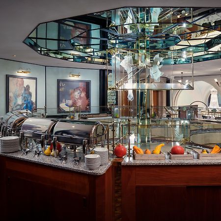 Art Nouveau Palace Hotel Praga Zewnętrze zdjęcie The photo shows a luxurious restaurant interior featuring a central buffet area. The buffet is set on a polished wooden counter with a granite surface, displaying several chafing dishes. Above the buffet, there is an eye-catching mirrored structure t