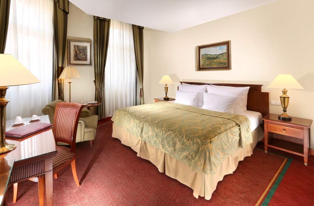 Art Nouveau Palace Hotel Praga Zewnętrze zdjęcie The photo shows the interior of a hotel room. It features a neatly made bed with a light green bedspread and white pillows. To the side, there's a bedside table with a lamp. A painting hangs on the wall above the bed, depicting a landscape. The room 